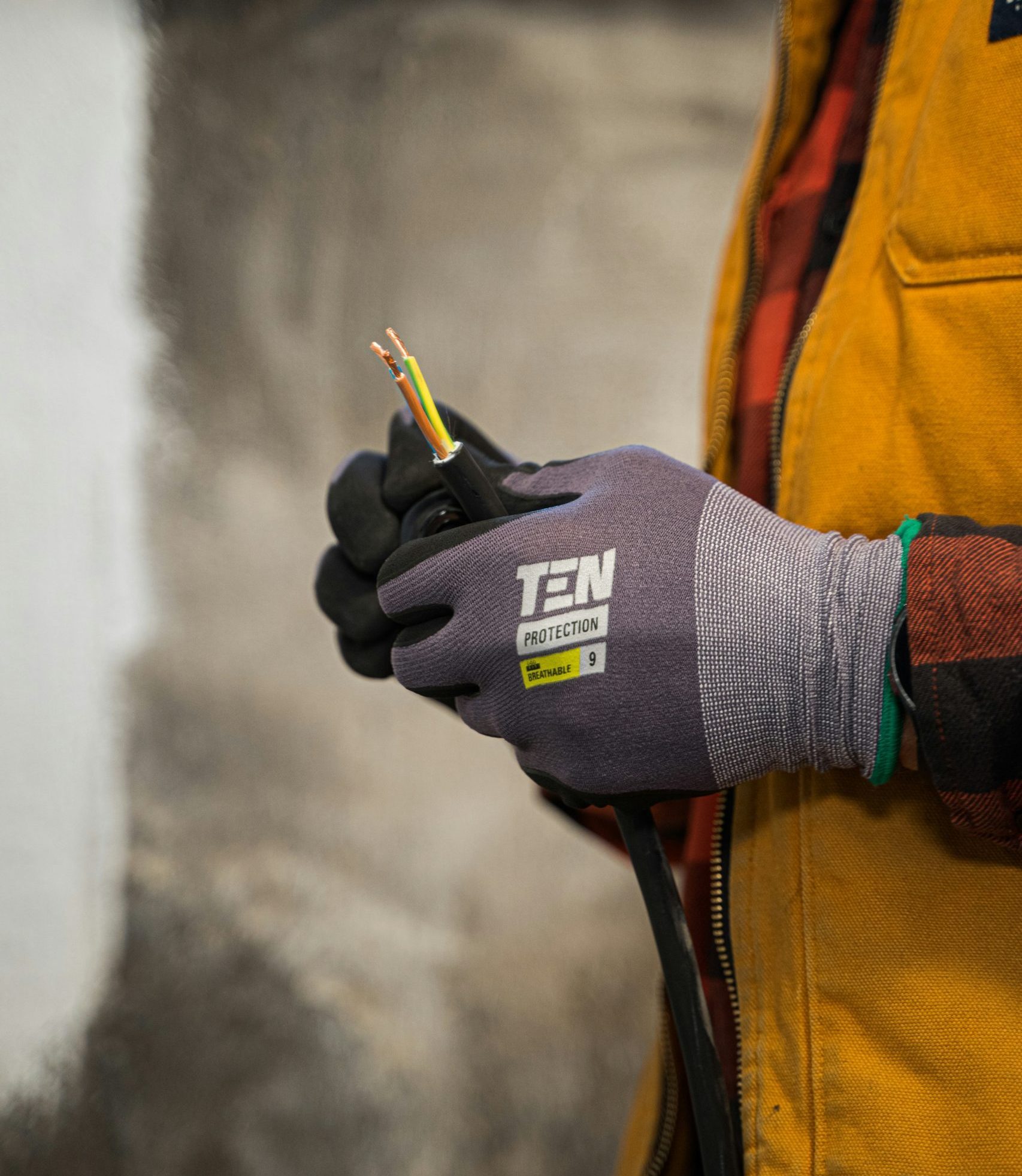 Person wearing protective gloves holding electrical wires, emphasizing safety and professionalism in electrical work, relevant to selling electrical businesses and addressing industry challenges.