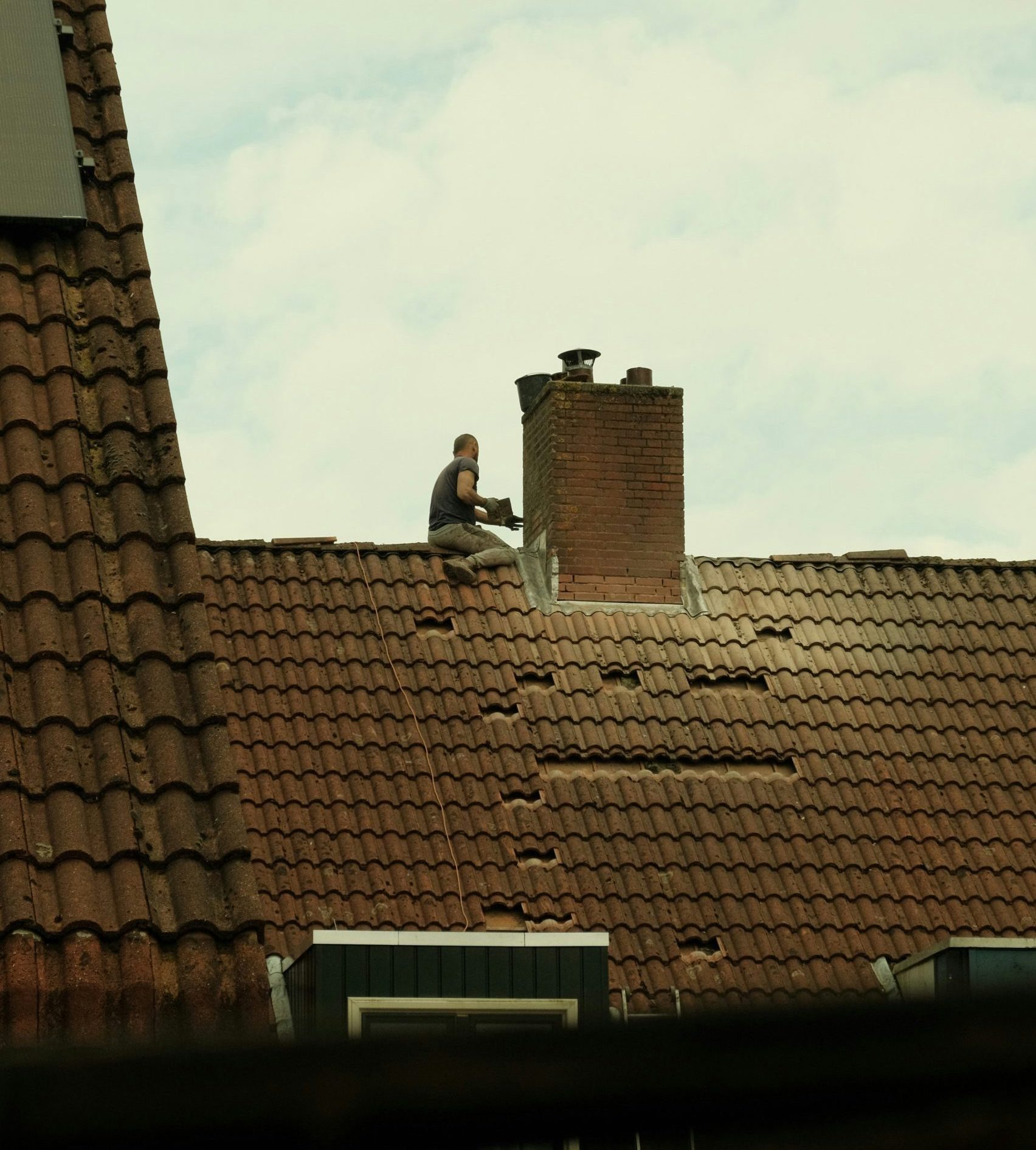 Roofer repairing chimney on a residential roof, highlighting the specialized work involved in roofing maintenance and the unique challenges faced by roofing business owners.