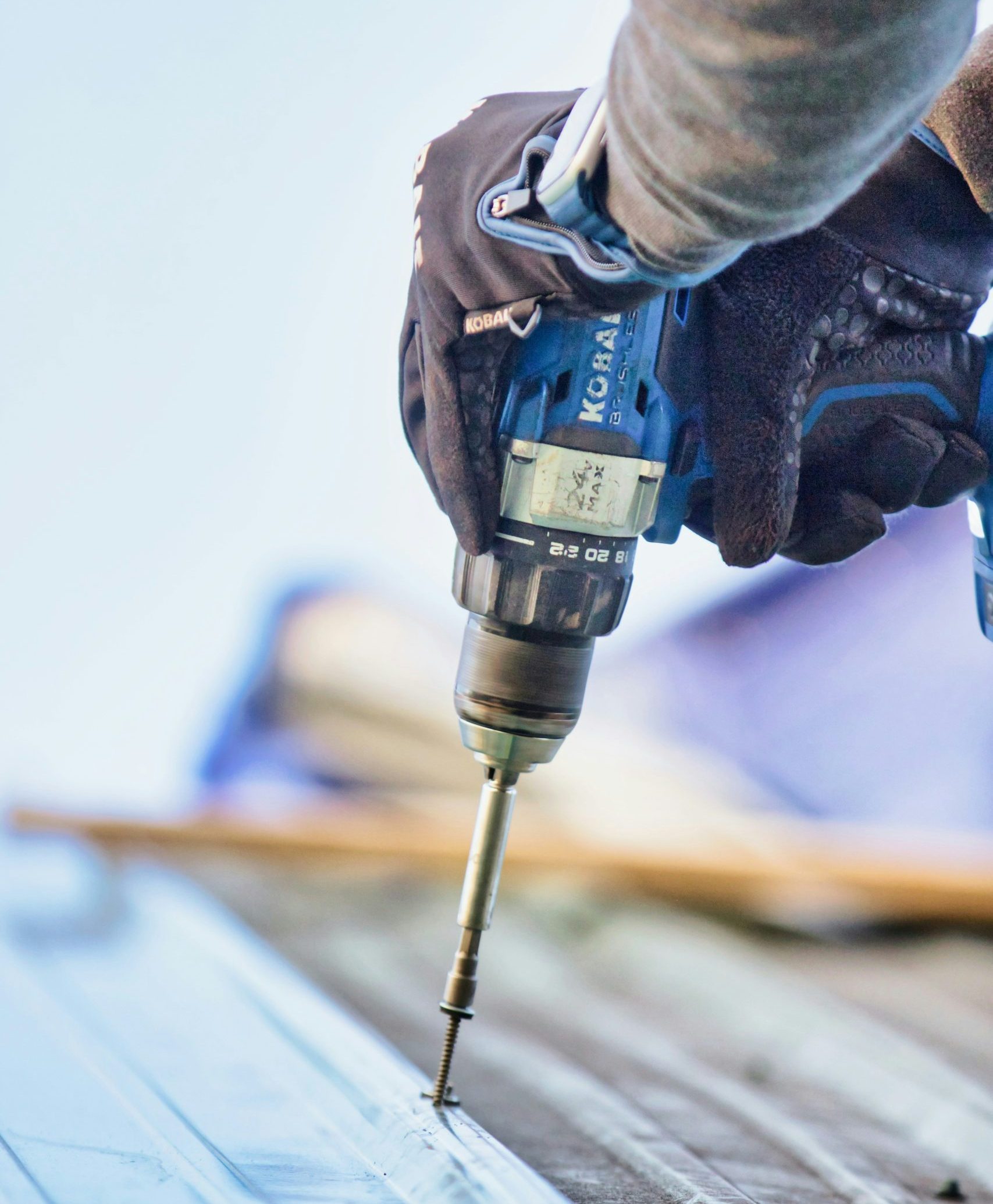 Worker using a Kobalt drill to secure roofing materials, emphasizing the hands-on skills essential in the roofing industry.