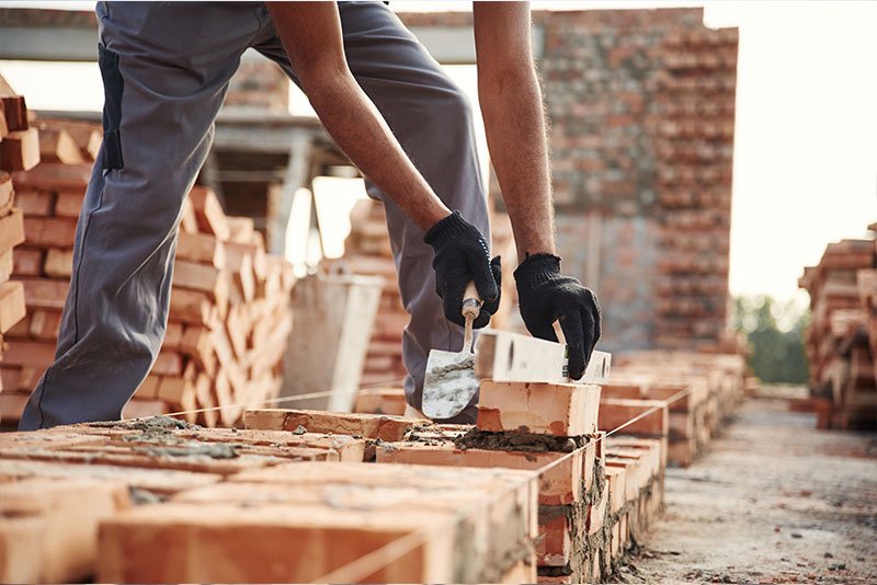 Construction worker laying bricks on a building site, showcasing masonry skills and construction activity relevant to construction and manufacturing businesses for sale.