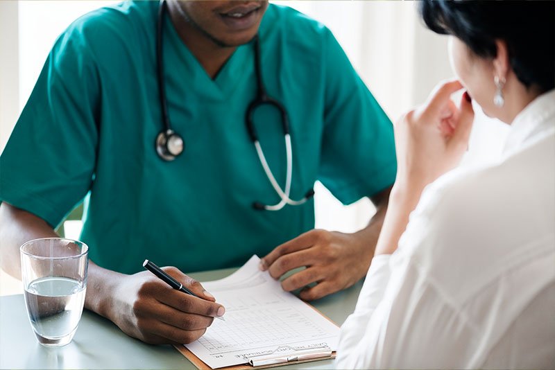 Healthcare professional in teal scrubs consulting with a patient, taking notes on a clipboard, emphasizing the demand for healthcare business services in Texas.