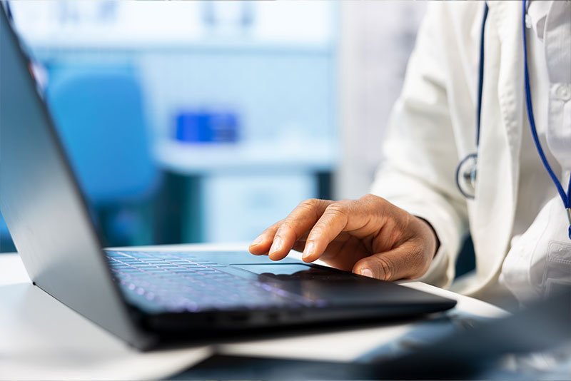 Healthcare professional using laptop in clinical setting, emphasizing technology in healthcare business transactions.