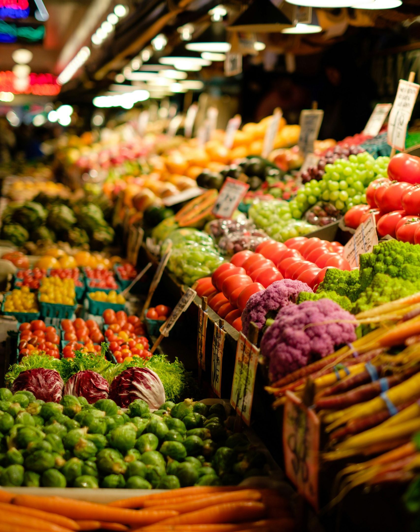 Vibrant display of fresh produce at a grocery market, featuring tomatoes, grapes, carrots, and various greens, highlighting the diverse offerings important for grocery store valuation and sales strategies.