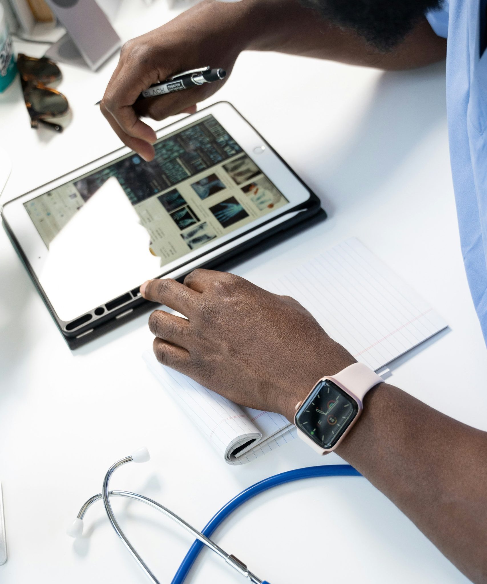 Healthcare professional using tablet and notepad, analyzing patient data and compliance metrics, stethoscope nearby, emphasizing operational infrastructure and clinical staffing in healthcare business evaluations.