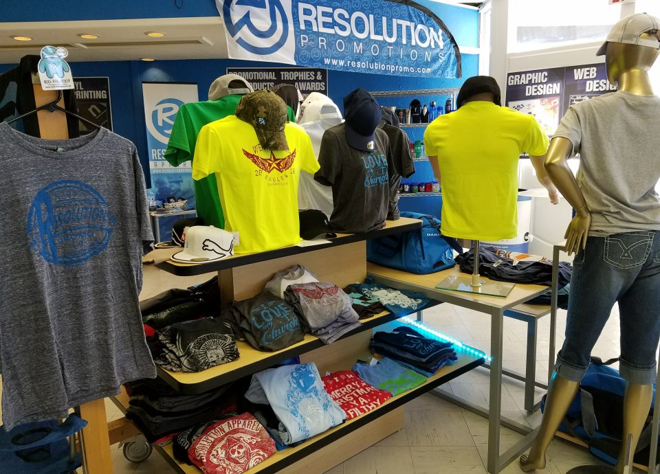 Display of colorful promotional apparel, including t-shirts and caps, at Resolution Promotions store, showcasing custom design services and merchandise for businesses.
